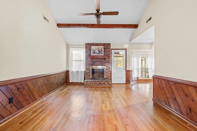 unfurnished living room with a wainscoted wall, beamed ceiling, a ceiling fan, and visible vents