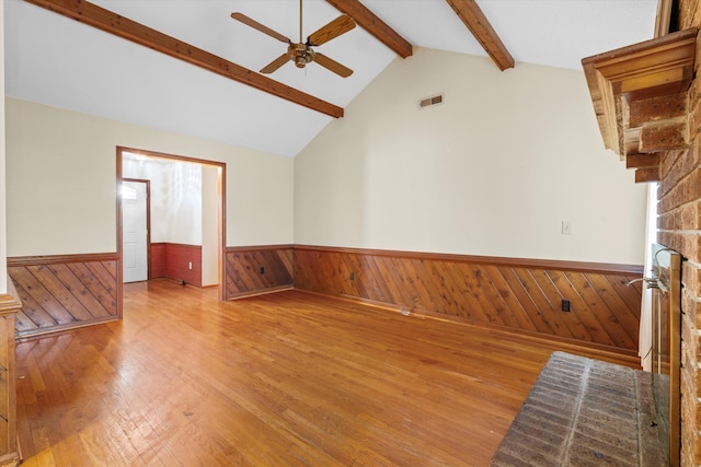 unfurnished living room with visible vents, vaulted ceiling with beams, a wainscoted wall, a fireplace, and a ceiling fan