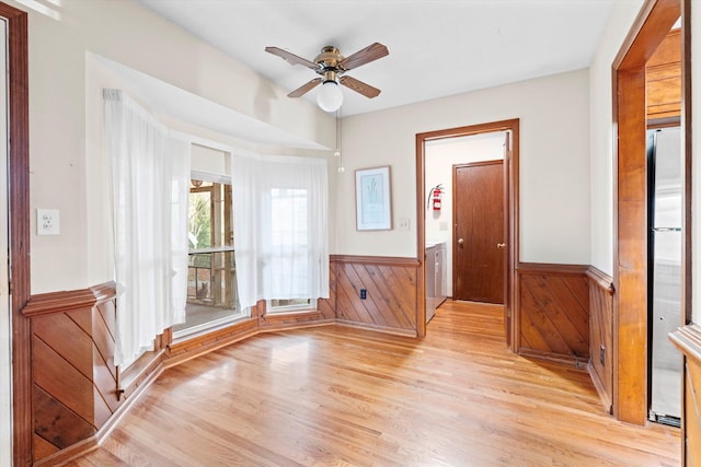 unfurnished room featuring wooden walls, a ceiling fan, a wainscoted wall, and light wood-type flooring