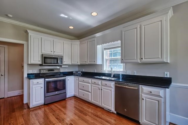 kitchen with stainless steel appliances, ornamental molding, light wood-type flooring, and white cabinetry