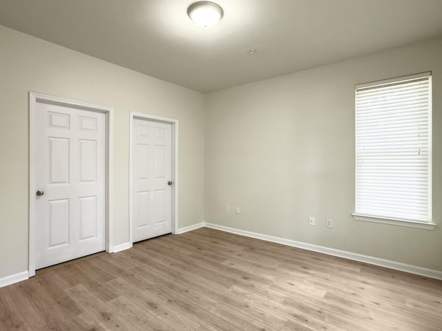 unfurnished bedroom with baseboards, multiple windows, and light wood-style flooring