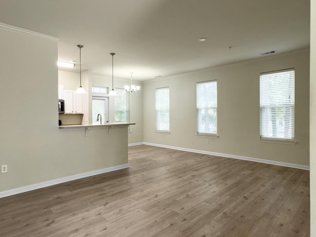 unfurnished living room featuring wood finished floors, ornamental molding, baseboards, visible vents, and a notable chandelier