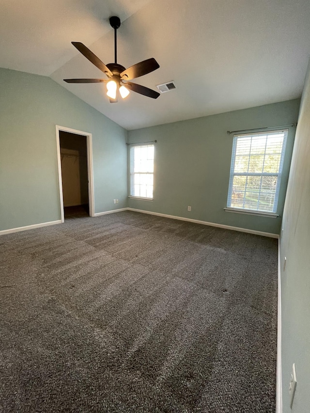 empty room with vaulted ceiling, dark colored carpet, and ceiling fan