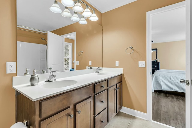 ensuite bathroom with tile patterned flooring, double vanity, baseboards, and a sink