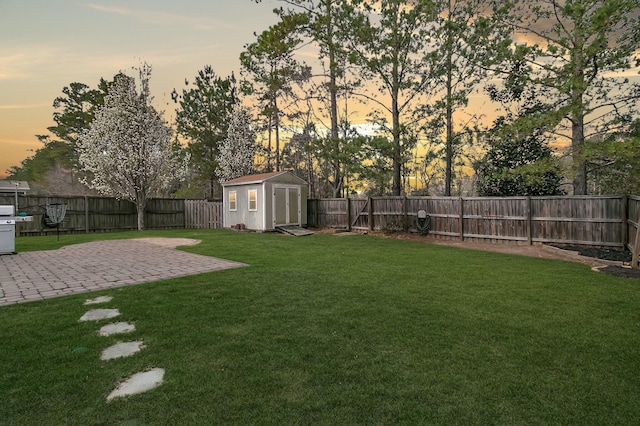 yard at dusk featuring a storage unit, an outbuilding, a fenced backyard, and a patio area