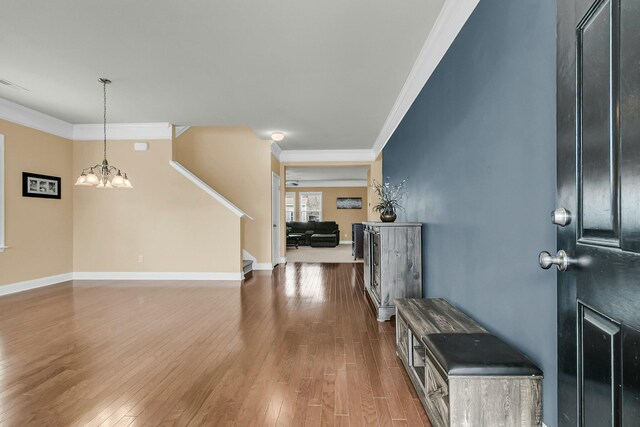 entryway featuring wood finished floors, crown molding, baseboards, a chandelier, and stairs