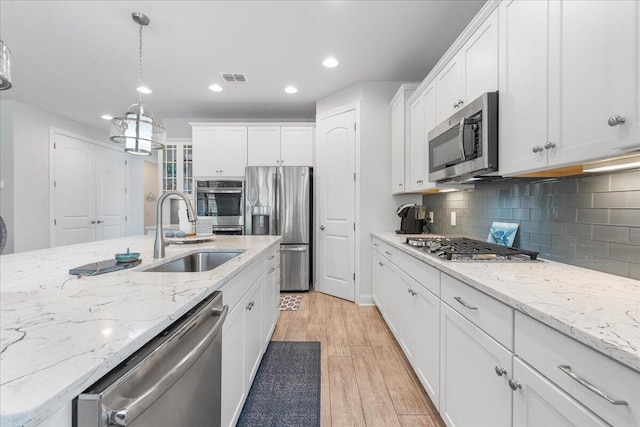 kitchen with sink, light hardwood / wood-style flooring, appliances with stainless steel finishes, pendant lighting, and white cabinets