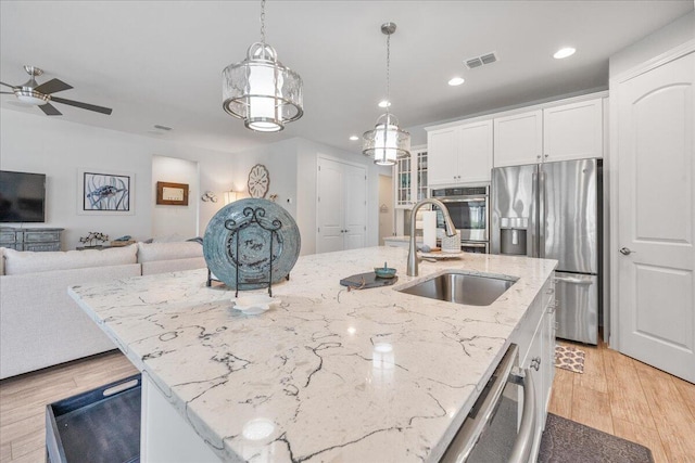 kitchen with sink, white cabinetry, decorative light fixtures, stainless steel appliances, and a kitchen island with sink