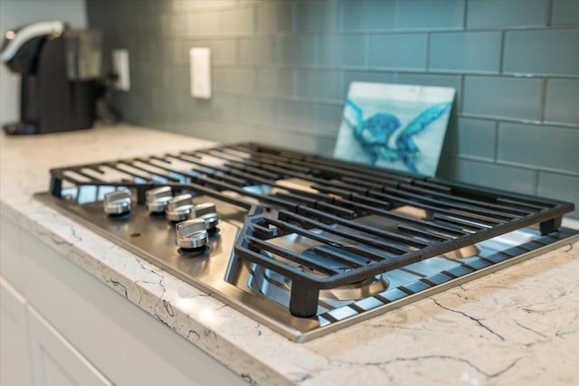 interior details with light stone counters, stainless steel gas stovetop, and backsplash