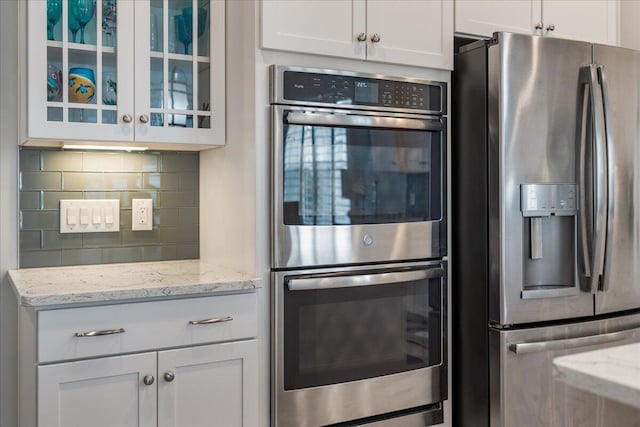 kitchen featuring white cabinetry, appliances with stainless steel finishes, light stone counters, and backsplash