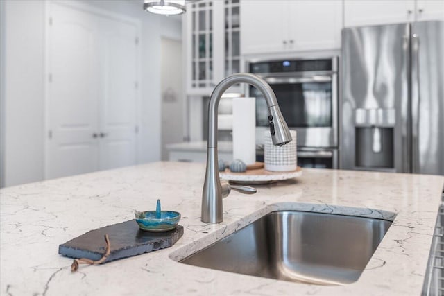 interior details featuring light stone counters, appliances with stainless steel finishes, sink, and white cabinets