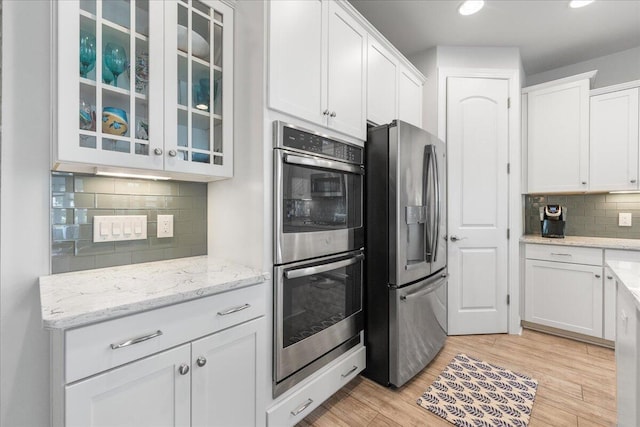 kitchen with tasteful backsplash, stainless steel appliances, light stone countertops, light hardwood / wood-style floors, and white cabinets