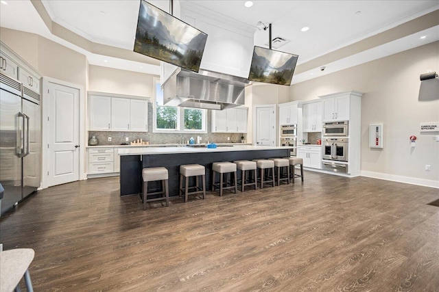 kitchen with a breakfast bar, a high ceiling, white cabinets, a kitchen island, and exhaust hood