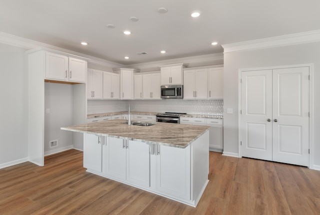 kitchen with a sink, stainless steel appliances, white cabinets, light wood-style floors, and crown molding