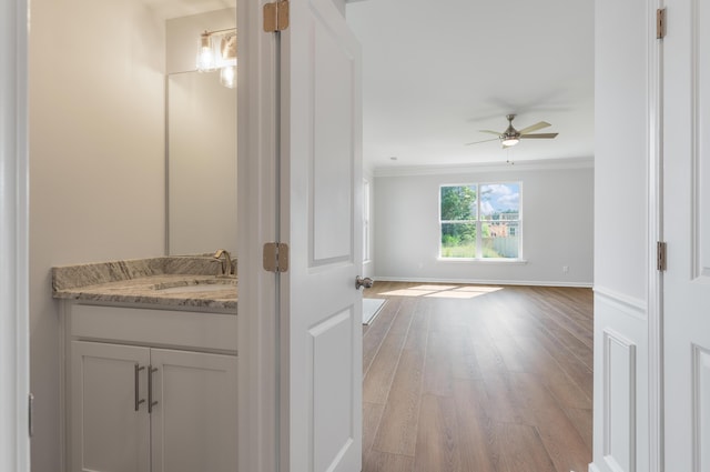 bathroom with ornamental molding, wood finished floors, baseboards, ceiling fan, and vanity