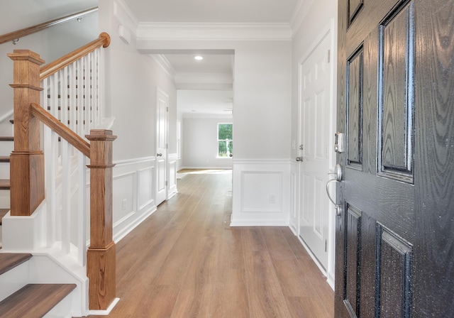 foyer entrance with wainscoting, wood finished floors, crown molding, and a decorative wall