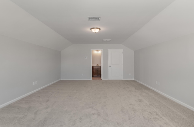 additional living space featuring lofted ceiling, baseboards, visible vents, and light carpet