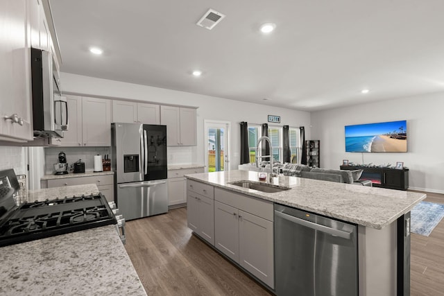 kitchen featuring appliances with stainless steel finishes, a sink, tasteful backsplash, open floor plan, and a kitchen island with sink