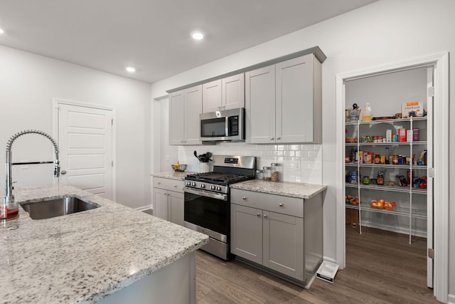 kitchen featuring stainless steel appliances, gray cabinets, a sink, dark wood finished floors, and decorative backsplash