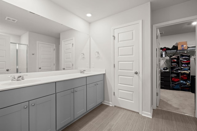 full bath featuring double vanity, a shower stall, baseboards, a walk in closet, and recessed lighting