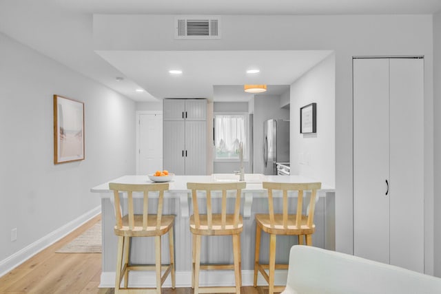 kitchen with freestanding refrigerator, a peninsula, light wood-style flooring, a sink, and a breakfast bar area
