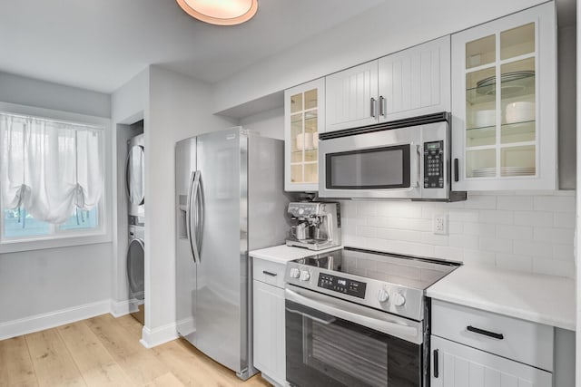 kitchen with appliances with stainless steel finishes, stacked washer and clothes dryer, light wood-style floors, decorative backsplash, and light countertops