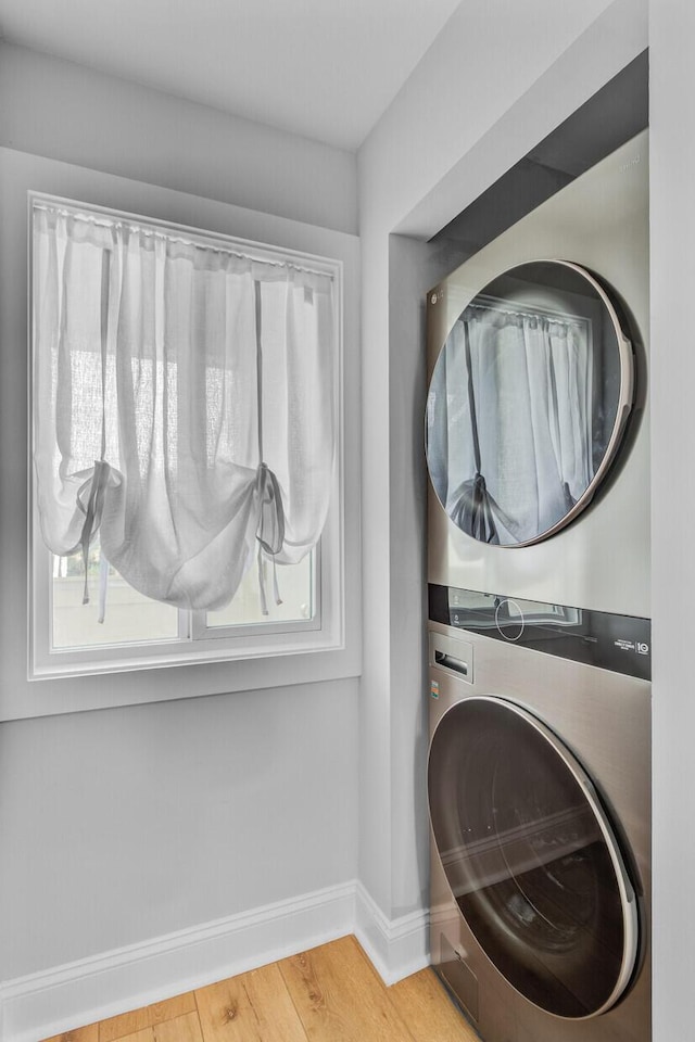 clothes washing area featuring stacked washer and clothes dryer, baseboards, and wood finished floors