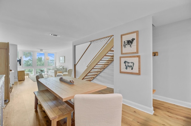 dining space featuring stairs, light wood-type flooring, and baseboards