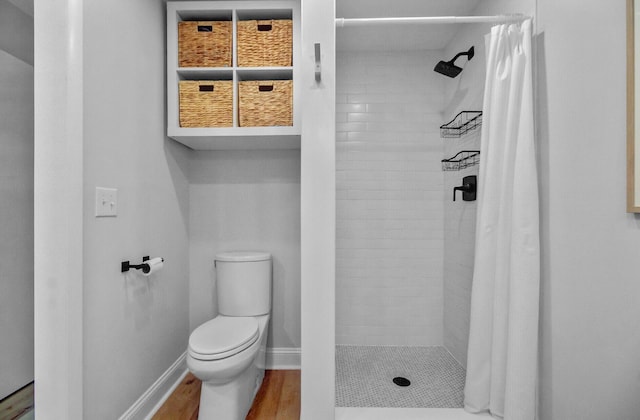 bathroom with toilet, a stall shower, wood finished floors, and baseboards