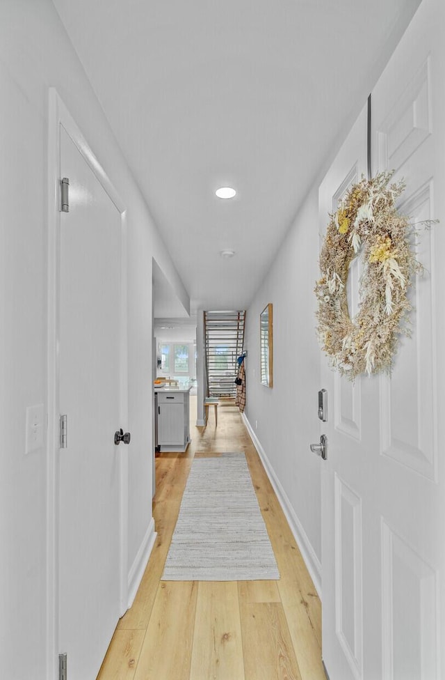 hallway featuring light wood finished floors, baseboards, and recessed lighting