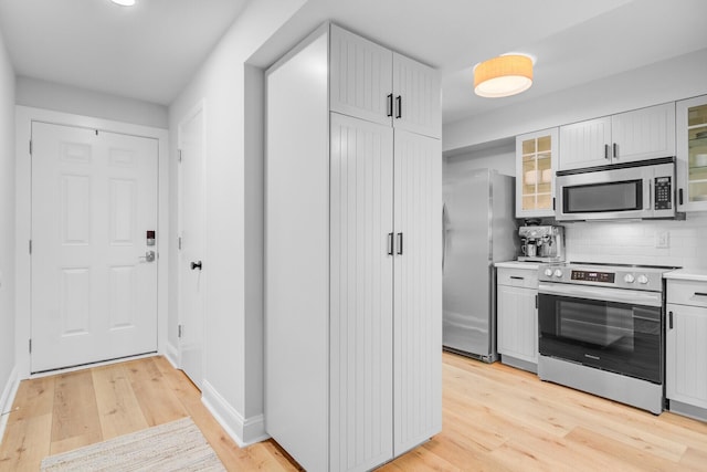 kitchen with stainless steel appliances, light wood-style floors, tasteful backsplash, light countertops, and glass insert cabinets