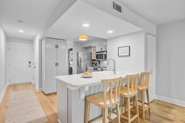 kitchen featuring stainless steel appliances, stacked washing machine and dryer, a kitchen breakfast bar, a peninsula, and light wood-style floors
