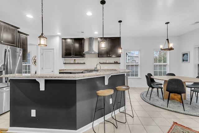 kitchen featuring light tile patterned floors, wall chimney exhaust hood, a kitchen bar, and stainless steel refrigerator with ice dispenser