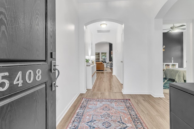 interior space with arched walkways, light wood-type flooring, visible vents, and baseboards