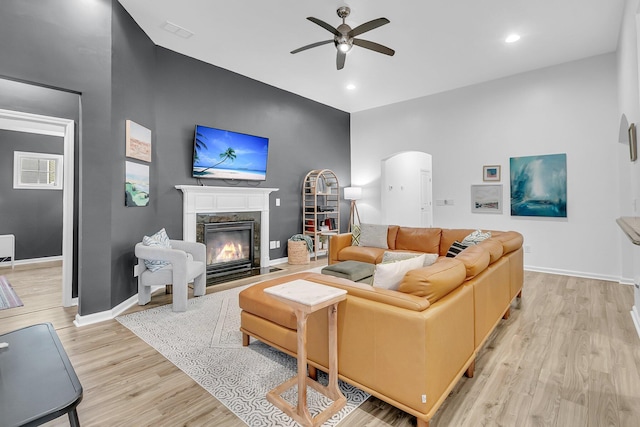 living room featuring arched walkways, ceiling fan, wood finished floors, a high end fireplace, and baseboards