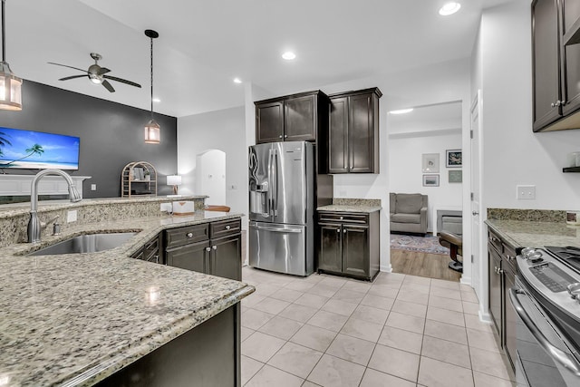 kitchen featuring arched walkways, ceiling fan, appliances with stainless steel finishes, light stone countertops, and a sink