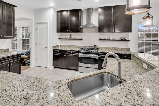 kitchen with light stone counters, a healthy amount of sunlight, stainless steel gas stove, a sink, and wall chimney range hood