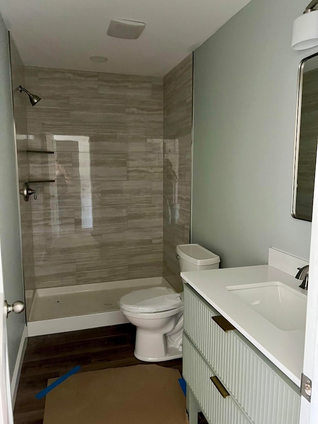 bathroom with toilet, vanity, hardwood / wood-style flooring, and tiled shower