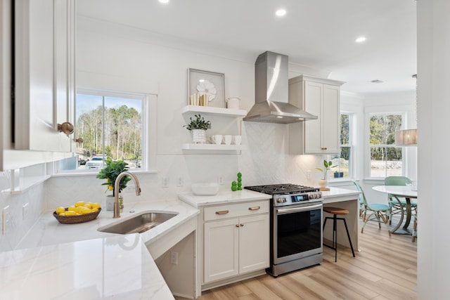 kitchen featuring sink, white cabinets, wall chimney exhaust hood, and stainless steel gas range