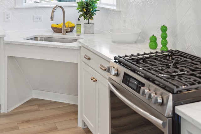 kitchen with light hardwood / wood-style flooring, sink, white cabinetry, stainless steel gas range oven, and light stone countertops