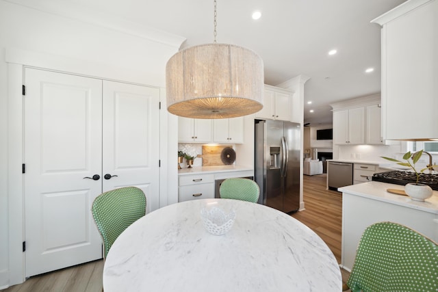 kitchen with white cabinetry, light wood-type flooring, stainless steel appliances, decorative light fixtures, and tasteful backsplash