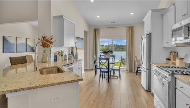 kitchen featuring light wood finished floors, light stone counters, a peninsula, stainless steel appliances, and backsplash