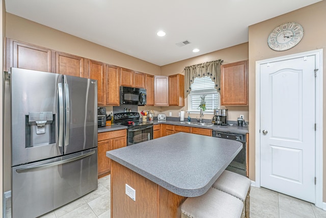 kitchen with visible vents, a center island, light tile patterned floors, black appliances, and a sink