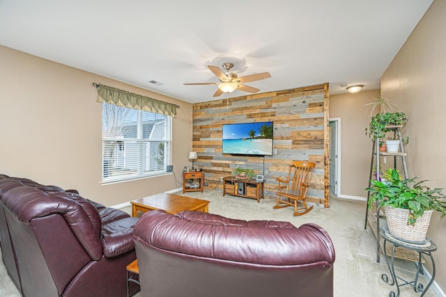 carpeted living area featuring visible vents, a ceiling fan, wooden walls, baseboards, and an accent wall