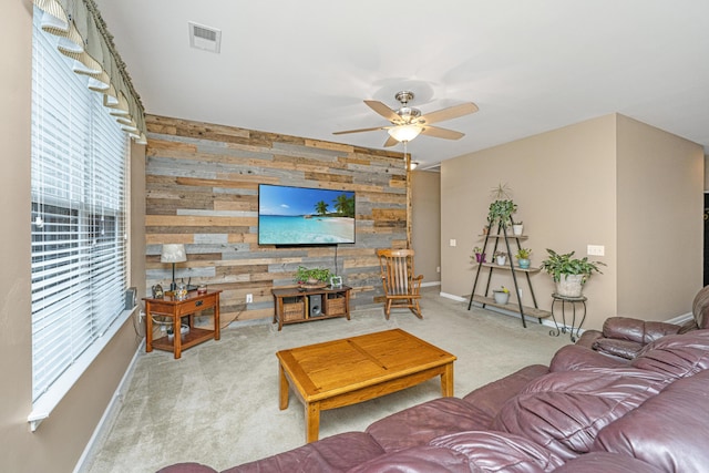 living room featuring wooden walls, carpet, baseboards, ceiling fan, and an accent wall