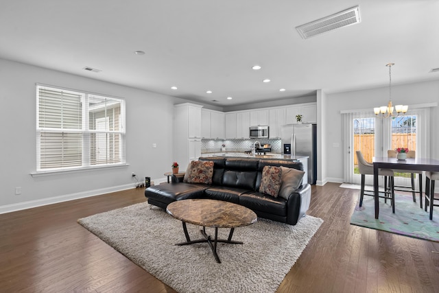 living room with dark wood-type flooring, an inviting chandelier, and sink