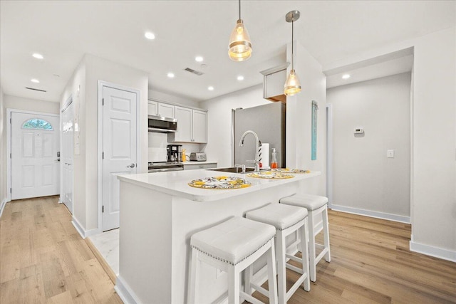 kitchen featuring decorative light fixtures, light hardwood / wood-style floors, white cabinetry, appliances with stainless steel finishes, and an island with sink