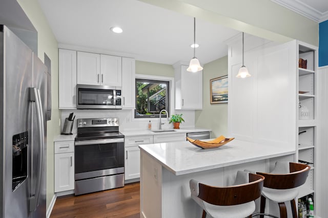 kitchen with a breakfast bar, white cabinets, sink, appliances with stainless steel finishes, and decorative light fixtures