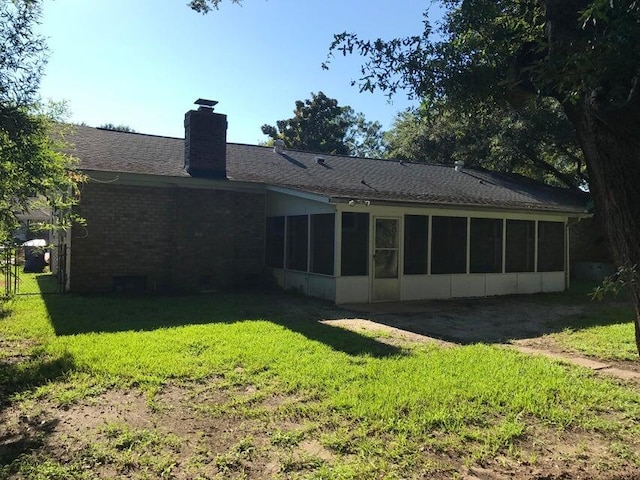 rear view of property with a sunroom, a yard, a chimney, and brick siding