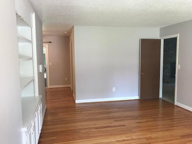spare room with light wood-type flooring, a textured ceiling, and baseboards